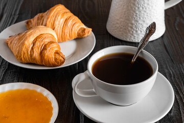 Coffee cup with croissant on a rustic dark wooden table. Food series. Two tasty fresh croissants, jam, orange juice. Continental breakfast served with freshly baked pastry. Close up view, Good morning