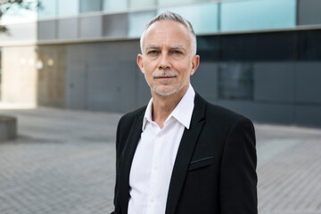 Portrait of a handsome senior businessman standing at outdoors. Mature corporate confident executive looking at camera. Financial concept 