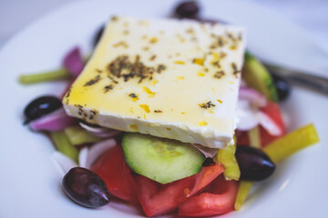Traditional fresh greek salad with vegetables, feta cheese, spices olives and olive oil on a plate served in traditional Greek cafe tavern restaurant in the street of Athens, Greece