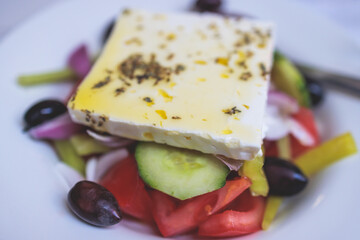Traditional fresh greek salad with vegetables, feta cheese, spices olives and olive oil on a plate served in traditional Greek cafe tavern restaurant in the street of Athens, Greece