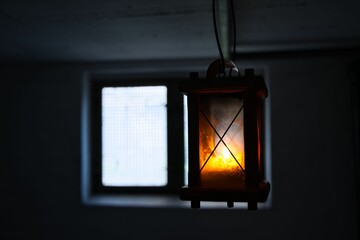 Closeup of a lit retro lantern, lamp hanging in front of a window