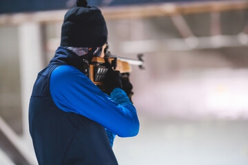 Biathlete with rifle on a shooting range during biathlon training, skiers on training ground in winter snow, athletes participate in biathlon competition on slope piste