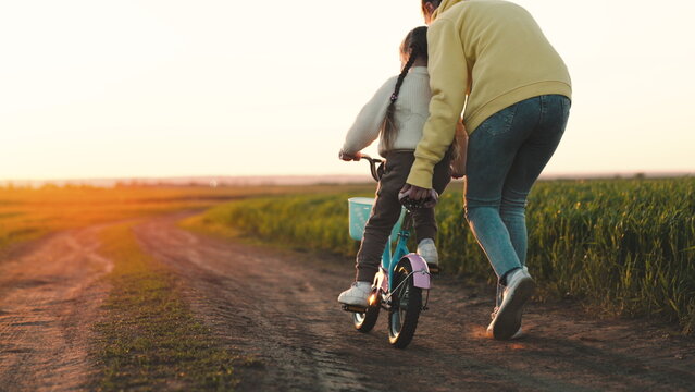 mother rides child bicycle sunset. happy family park. Mom teaches her daughter ride bike. concept happy family summer park. fun vacation. teamwork. mother runs green grass rolling child bicycle
