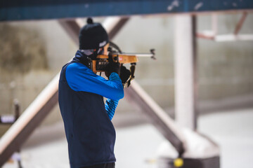 Biathlete with rifle on a shooting range during biathlon training, skiers on training ground in winter snow, athletes participate in biathlon competition on slope piste