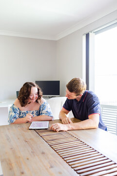Male NDIS provider assisting young woman with down syndrome using tablet