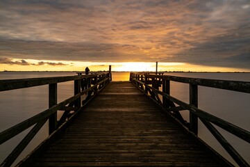 Pier leading to a calm sea under the golden glow of sunset in a cloudy sky