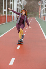 Obraz premium Funny free hipster Woman with dreadlocks on longboard on the road riding in the city at her 30s. female with bright colorful hair enjoy outdoor active lifestyle, play extreme sport