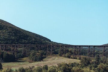 Big railway bridge surrounded by green trees with hills and the blue sky in the background