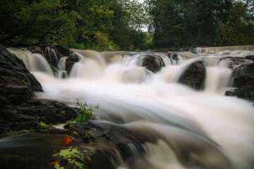 Long exposure shot of a cascade waterfall coming down the big rocks in a green forest