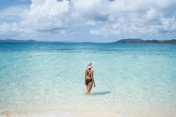 Vacation on the seashore. Back view of young woman in hat bathing on the beautiful tropical white sand beach.