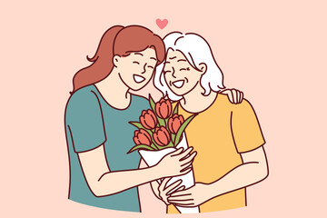 Woman hugs elderly mother and gives bouquet of flowers congratulating with birthday or mother day and thanks for good upbringing. Grown up daughter takes care of mother of retirement age 