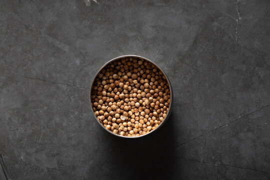Spice tin of coriander seeds on dark marble background