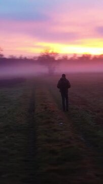 Drone shot of a Caucasian professional photographer walking in a green field taking photos at sunset