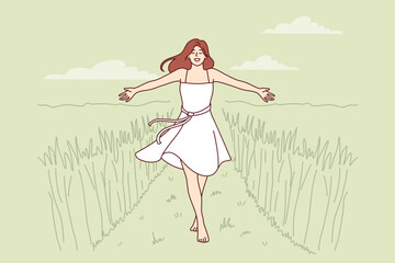 Woman walks along path among tall grass enjoying beautiful nature in rural or farming area. Girl in dress enjoys walk in wild nature or agricultural field in ecologically clean place. 