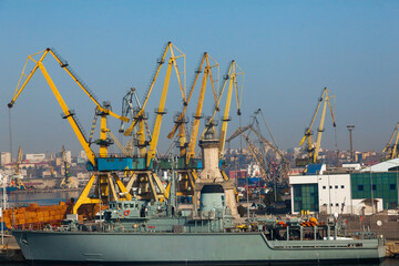 A Romanian Navy ship is moored at the pier in the port of Constanta near harbor cranes and port facilities.