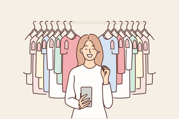 Woman with phone near hanger with T-shirts rejoices sale and opportunity to buy clothes at discounts