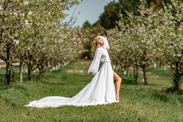 Blond blooming garden. A woman in a white dress walks through a blossoming cherry orchard. Long dress flies to the sides,