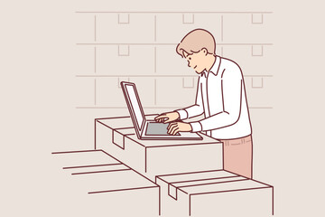 Man with laptop works in warehouse, standing near boxes, auditing availability of goods in storage