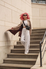 Portrait shooting of a stylish girl with pink hair. Beige shades. Trends of spring and summer 2023.Beige Trench cloak with white top and pants. Black small belt bag