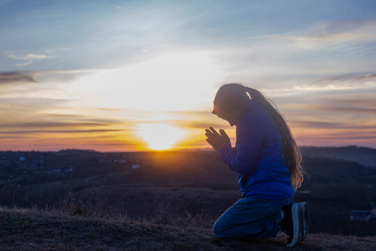 Girl on her knees. Prayer at sunset. Worship of God. Repentance for sins. On the knees