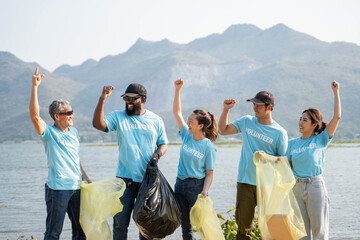 Happy Group of young volunteers helping to keep nature clean and picking up the garbage from a sandy shore.