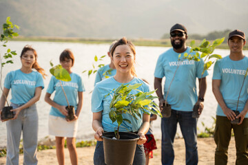Portrait of young woman with background Group of volunteer holding Pot With Green Plant Smiling To Camera Standing On river. Protection Of Environment And Nature, Ecology Concept.
