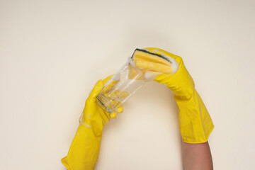 woman wearing yellow cleaning gloves on light color background cleaning glass cup with cleaning sponge