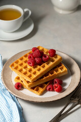 Breakfast waffles with berries in plate served with cup of tea.