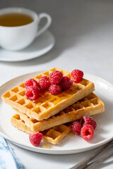 Breakfast waffles with berries in plate served with cup of tea.