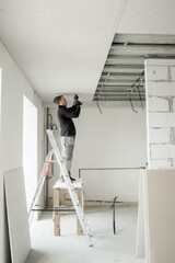 The worker attaches plasterboard on metal frame. Installation of ceiling - obrazy, fototapety, plakaty