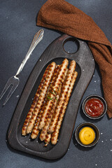 Roasted pork meat sausages on wooden board. Set of sauces, traditional food for picnic or BBQ
