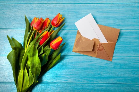 Top view of the tulip flowers with an envelope on the white wooden background