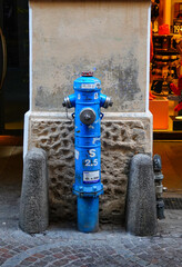 Ein blauer Wasserhydrant vor einer Betonsäule, zwischen zwei Betonpylonen, in der Laubengasse von Meran