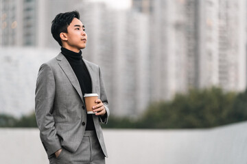 Asian businessman is drinking take away coffee outdoors in the city. 