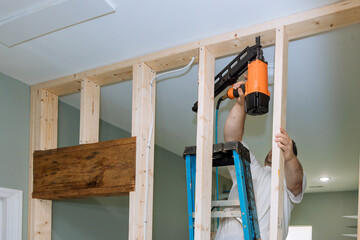 With help of an air hammer, builder nails wooden beams to frames house for construction