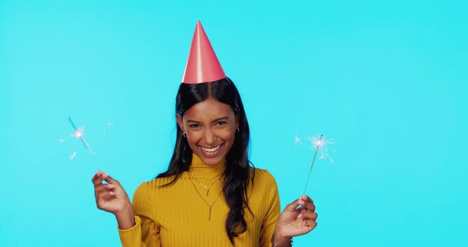Portrait, party and sparklers with a woman on a blue background in studio for a birthday celebration. Happy, smile and hat with an attractive young female celebrating or partying at a social event