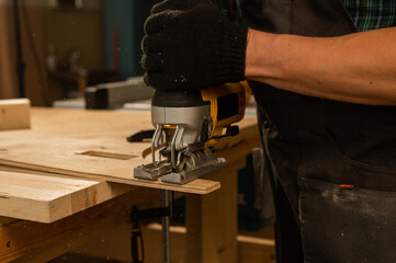 Man using electric jigsaw on wood in workshop. 