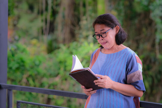 Asian woman standing alone in her home terrace reading a book
