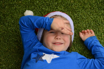 A boy in a Santa hat on a green background. The child lies on the floor, a portrait of a smiling...