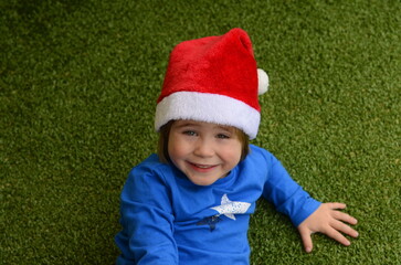 A boy in a Santa hat on a green background. The child lies on the floor, a portrait of a smiling...