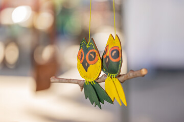 Colorful hanging ornament of a couple of owls made of leather and wood. Blurred background.