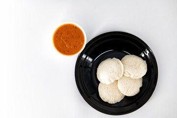 Hot and steaming idly in a black plate and tomato chutney  in a isolated white background. Steaming hot idly and red chutny isolated. Healthy food / Break fast in india.