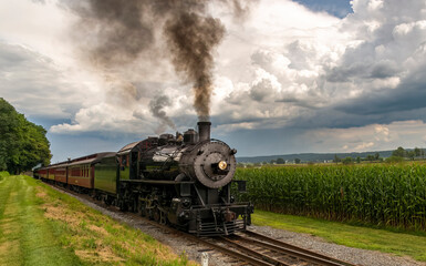 Fototapeta na wymiar Frontal View of Antique Passenger Train Approaching Blowing Black Smoke With Storm Clouds Approaching