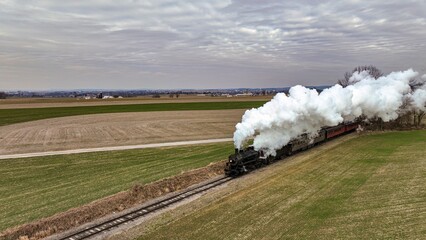 Obraz premium Aerial View of a Steam Passenger Train Approaching, Traveling Thru Open Farmlands, Blowing Lots of White Smoke