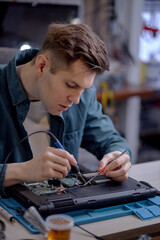 caucasian professional IT specialist replacing details in computer repair workshop, hardware upgrading. A real case of service assistance. Young male sit at work place repairing old laptop