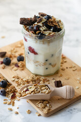 Yogurt with granola, blueberries, raspberries and honey in a jar on a wooden cutting board. Healthy breakfast.