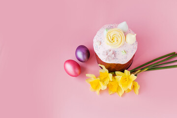 Traditional russian Easter ortodox cake with daffodil flower and colorful eggs on light pink background. Kulic, Kulich, Paska homemade bread with glaze. Spring christian holiday. Festive celebration