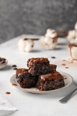 Chocolate brownies on a ceramic plate with pouring melted chocolate sauce on a light background....