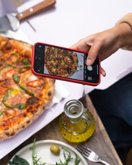 hand holding a phone to click a picture of pizza
