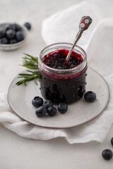 Blueberry jam in a glass jar with fresh berries on a white background.